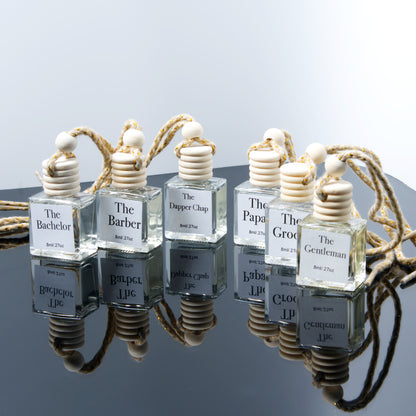 Set of hanging air diffuser glass bottles labeled with names like 'The Bachelor', 'The Barber', etc., on a reflective surface.