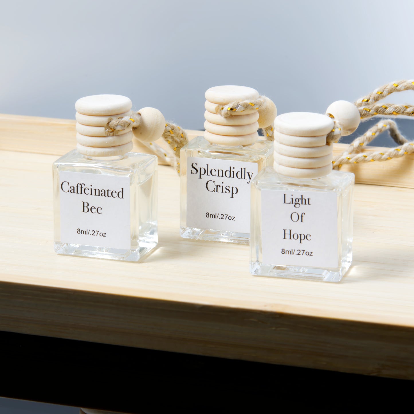 Three hanging air diffusers labeled 'Caffeinated Bee', 'Splendidly Crisp', and 'Light Of Hope' on a wooden surface.