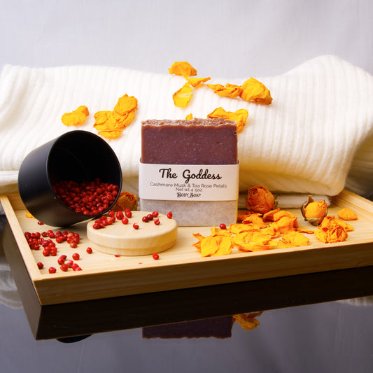 Bar of soap labeled 'The Goddess' on a wooden tray with decorative elements.
