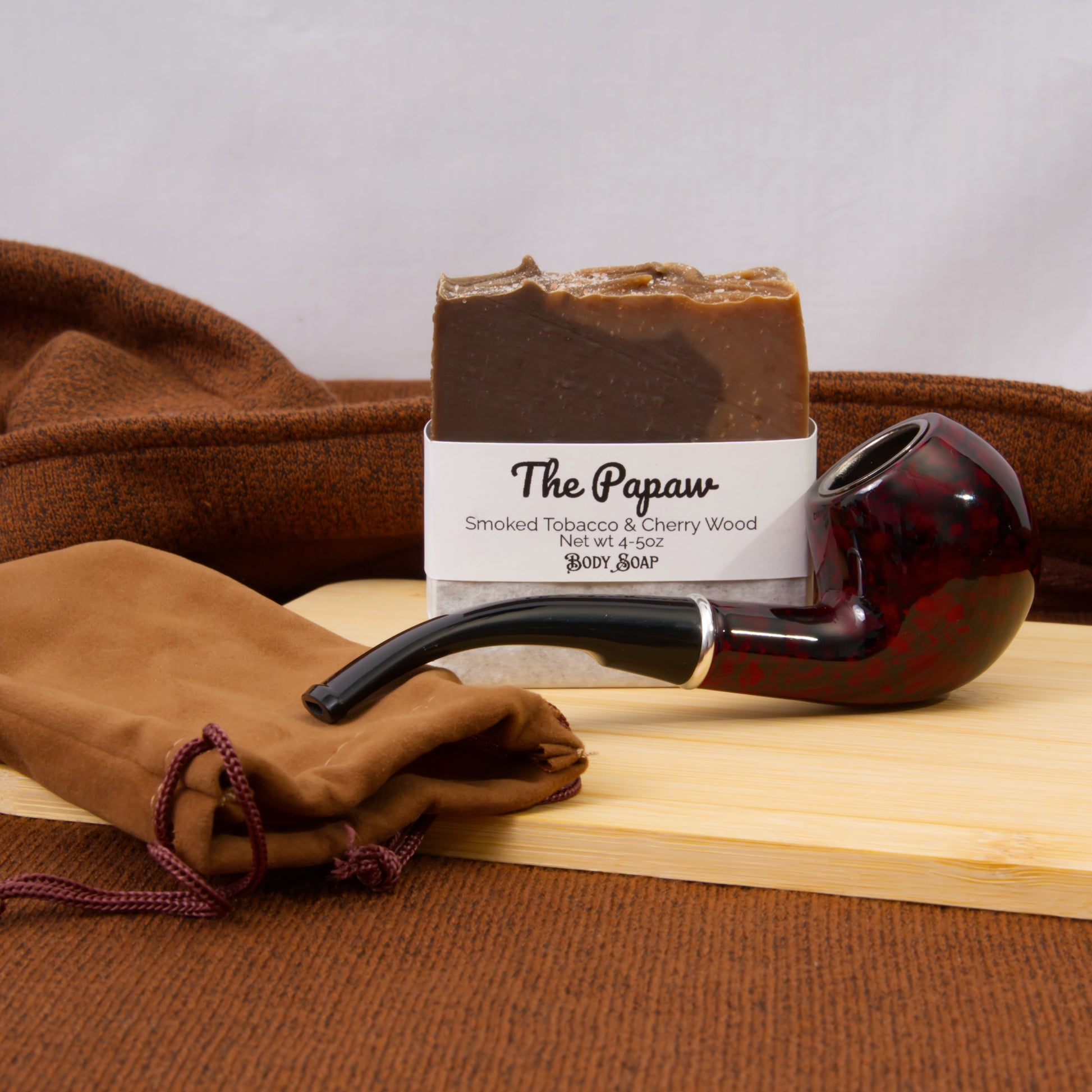 Bar of soap labeled 'The Papaw' with a smoking pipe and cloth on a wooden surface.