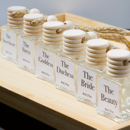 Set of hanging air diffuser glass bottles with wooden stoppers labeled 'The Sweetheart' to 'The Beauty' on a wooden surface.
