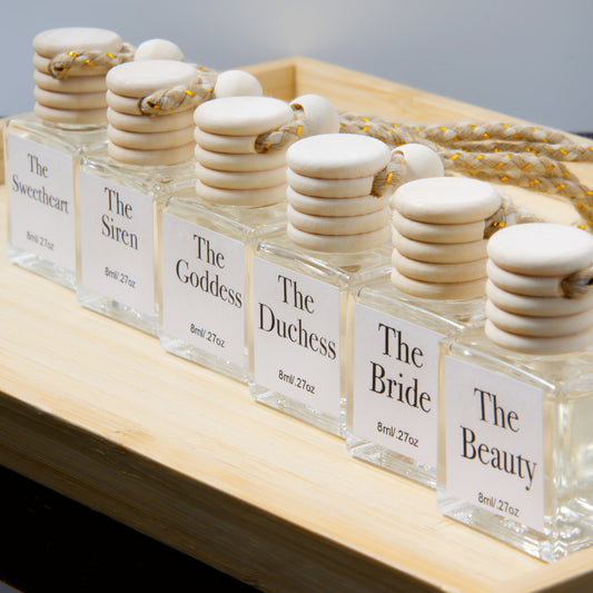 Set of hanging air diffuser glass bottles with wooden stoppers labeled 'The Sweetheart' to 'The Beauty' on a wooden surface.